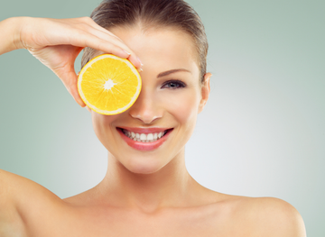 Frau mit Zitronenscheibe als Symbol für Vitamin C zur Reduktion von Pigmentflecken und für einen strahlenden Teint
